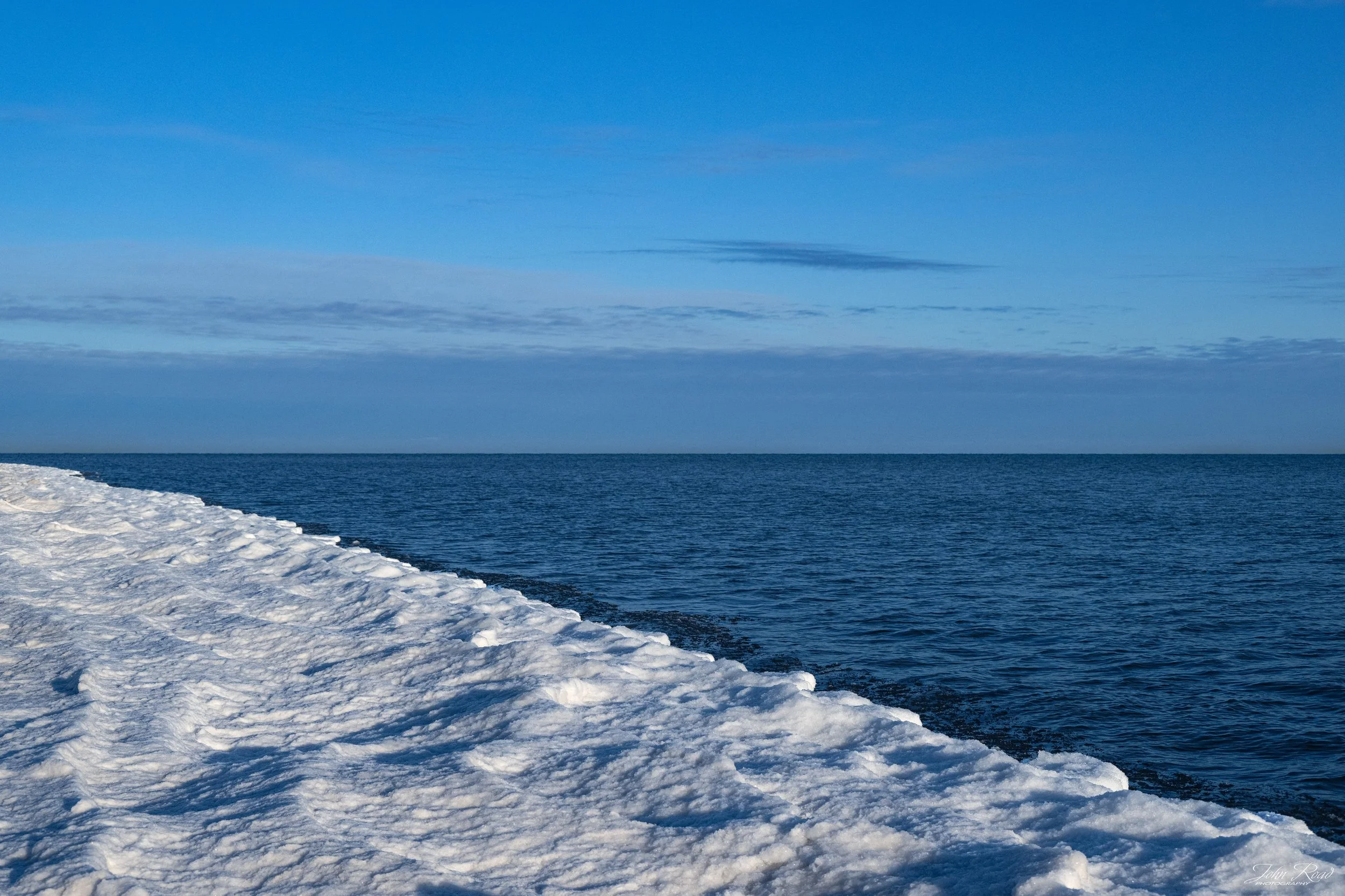 Frozen Lake Michigan shoreline with ice and snow under a blue winter sky