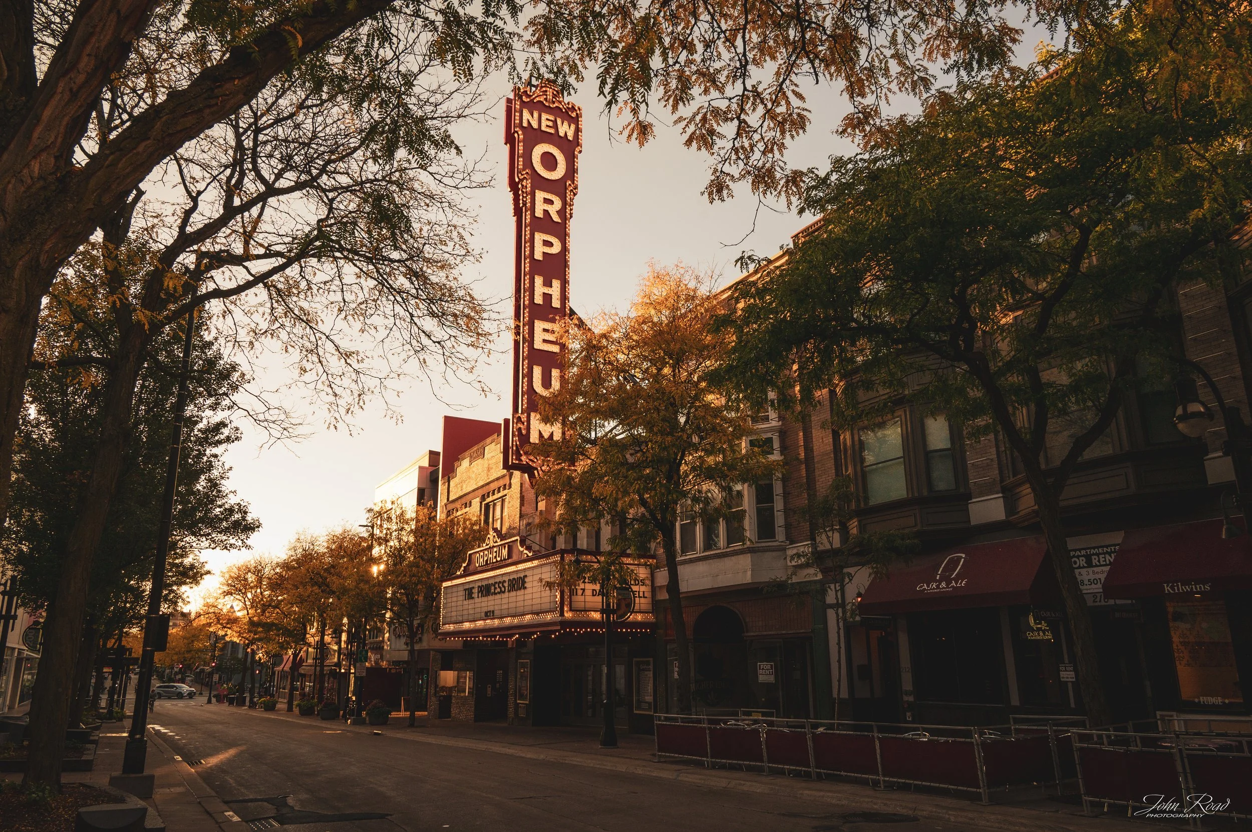 The Orpheum Theatre marquee on State Street in downtown Madison, Wisconsin, surrounded by autumn trees and illuminated by warm late-day sunlight.