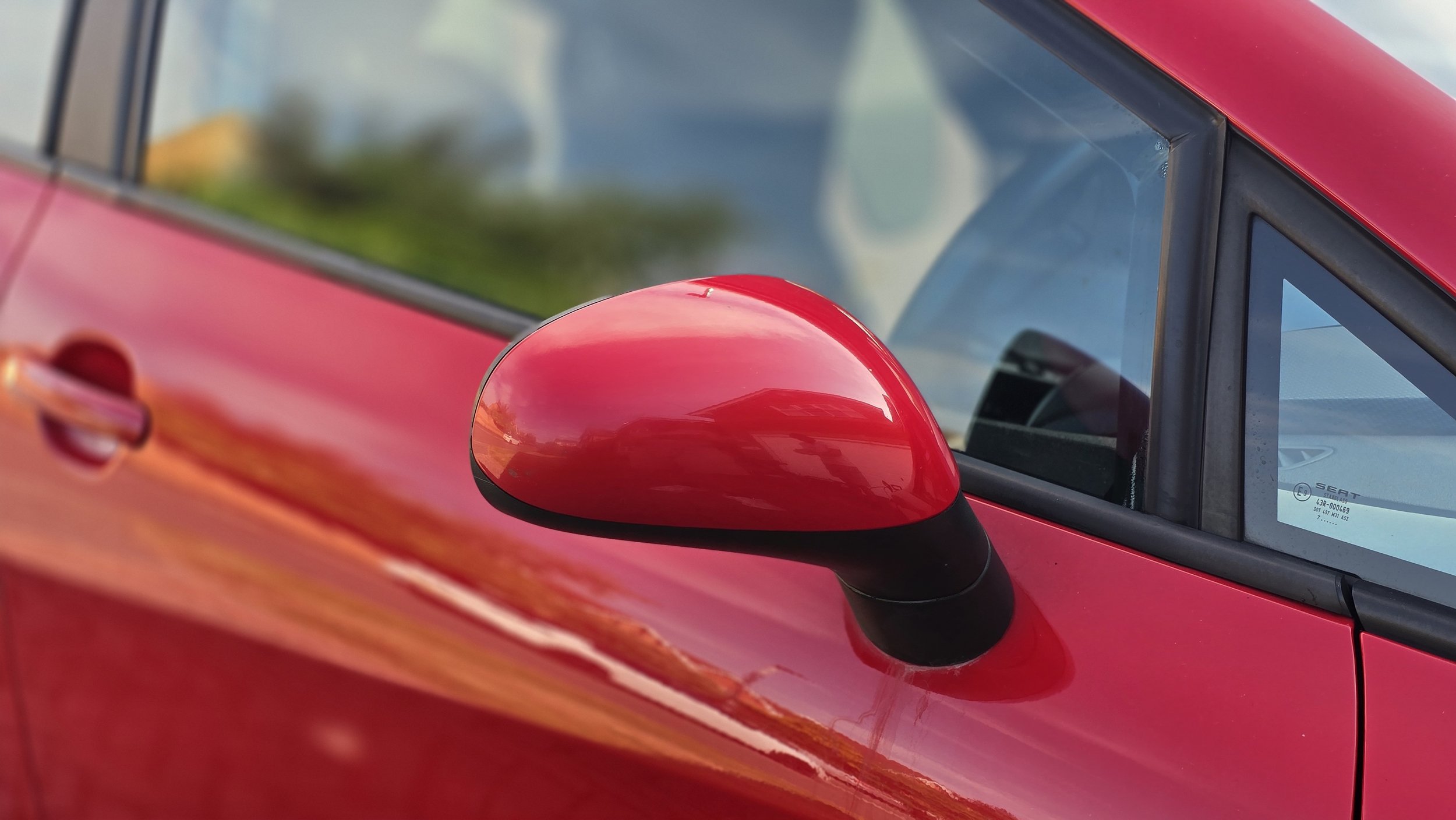 Close-up of a red car's side mirror and door window