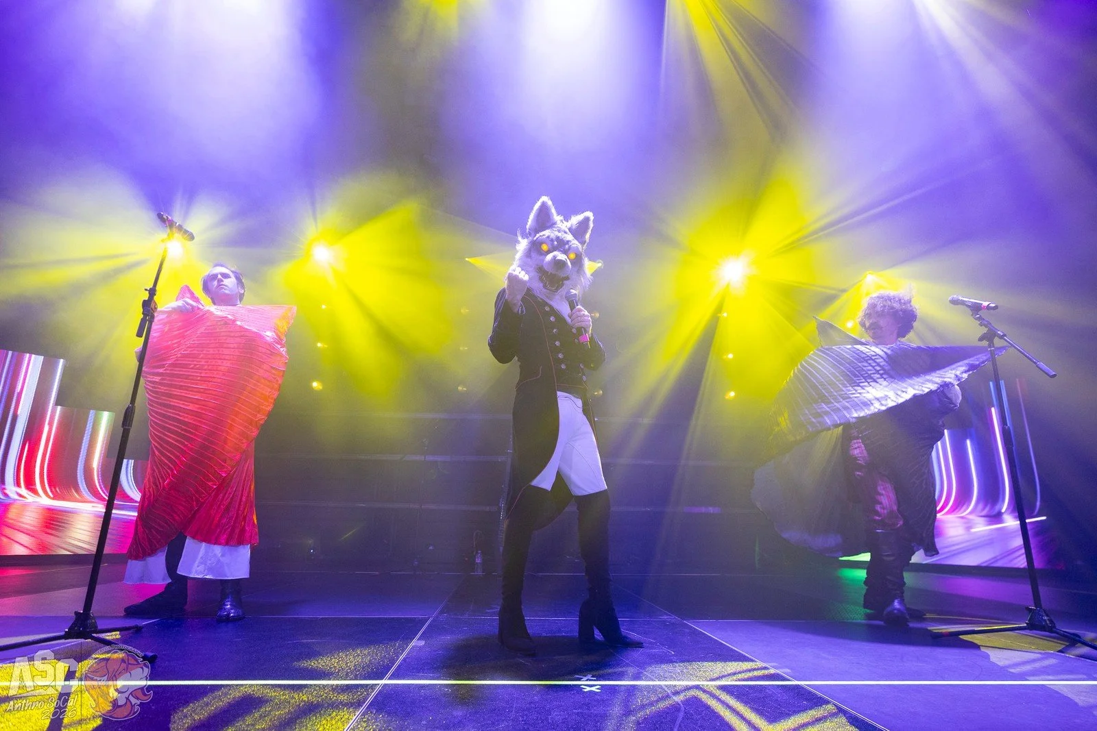 Pom, Chrono, and Charlie on stage, singing into microphones with colorful stage lights in the background. Bright yellow and purple lighting illuminate the scene.