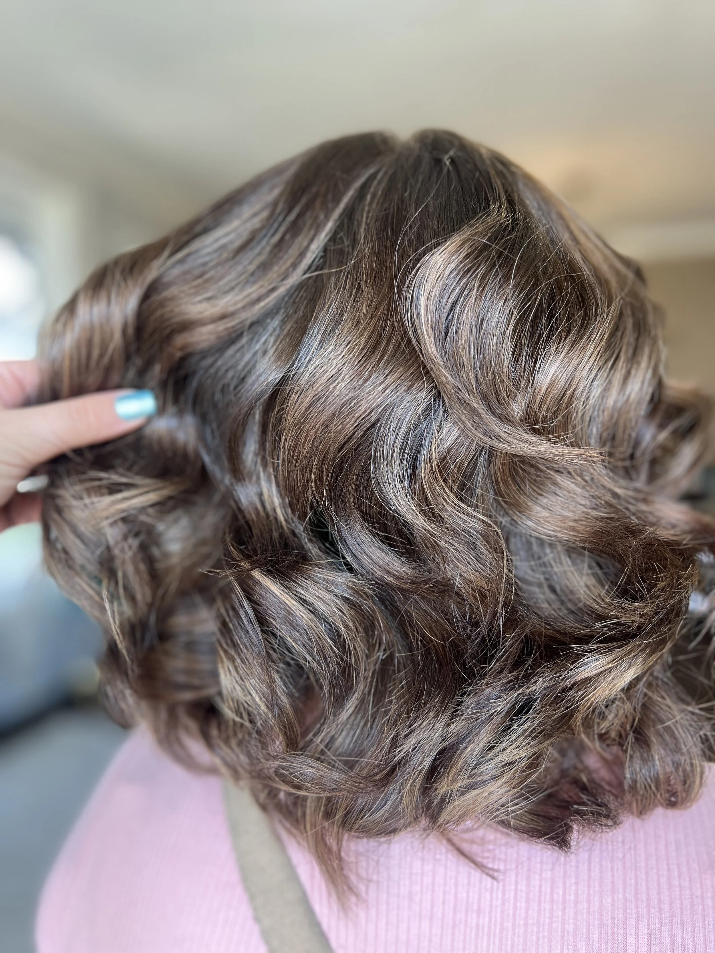 Close-up of a woman's brown, shoulder-length hair styled in loose curls.