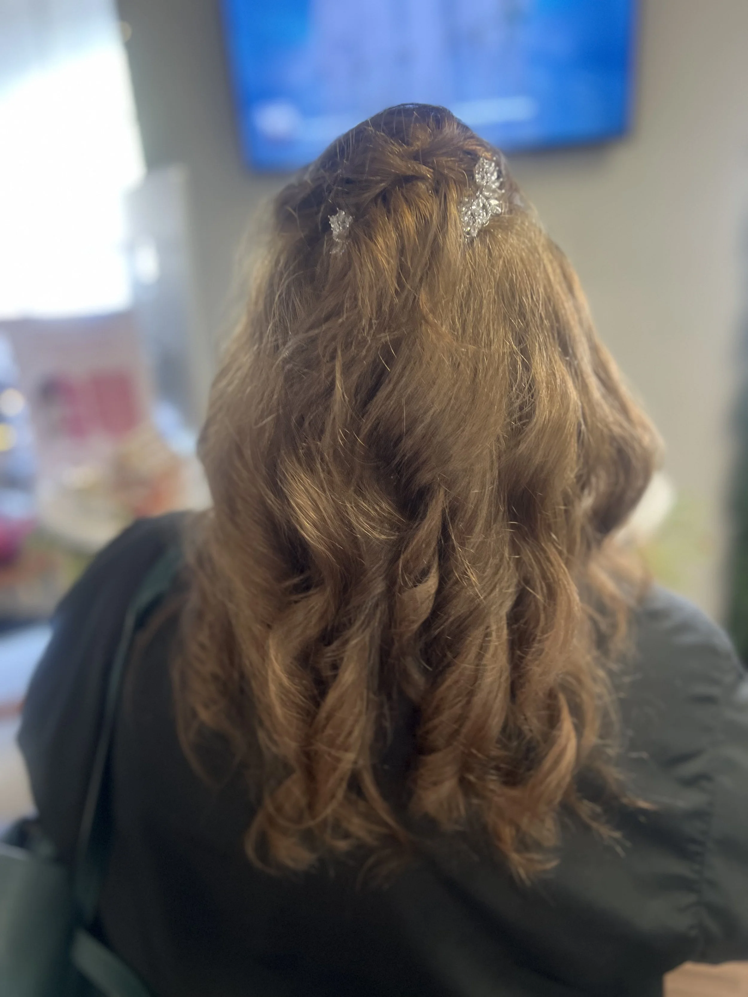 Back of a woman's head showing long, wavy, reddish-brown hair with decorative hair clips or accessories.