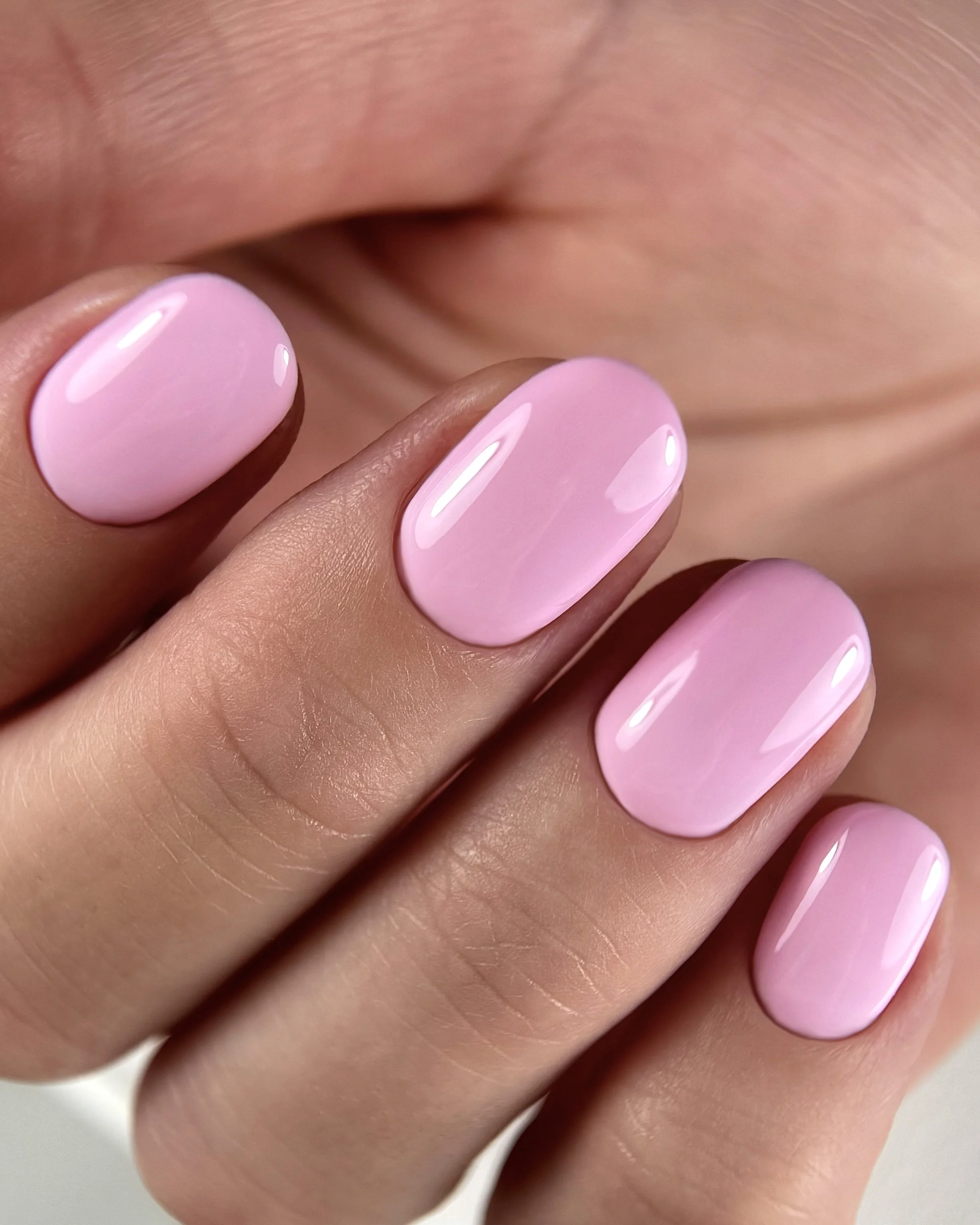 Close-up of a hand with manicured nails painted in light pink, glossy finish, against a blurred background.