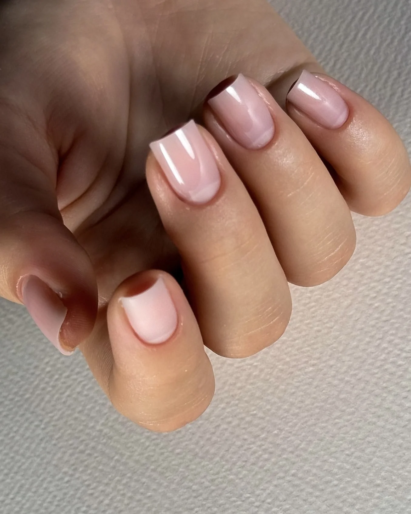 Close-up of a hand with manicured nails painted in a light pink color with a darker pink tip design.