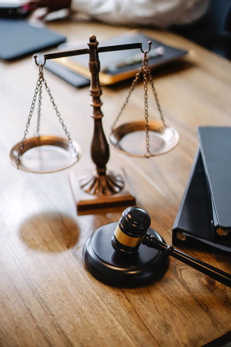 A wooden desk holding a judge's gavel, a set of balance scales, and a black file folder.