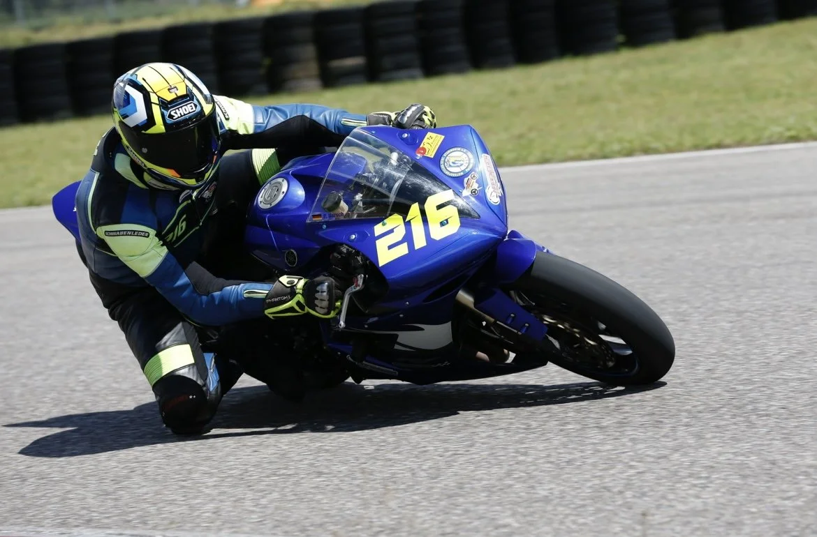 Motorradrennfahrer in Rennkleidung fährt auf einer Rennstrecke, Nummer 216 auf dem blauen Motorrad.