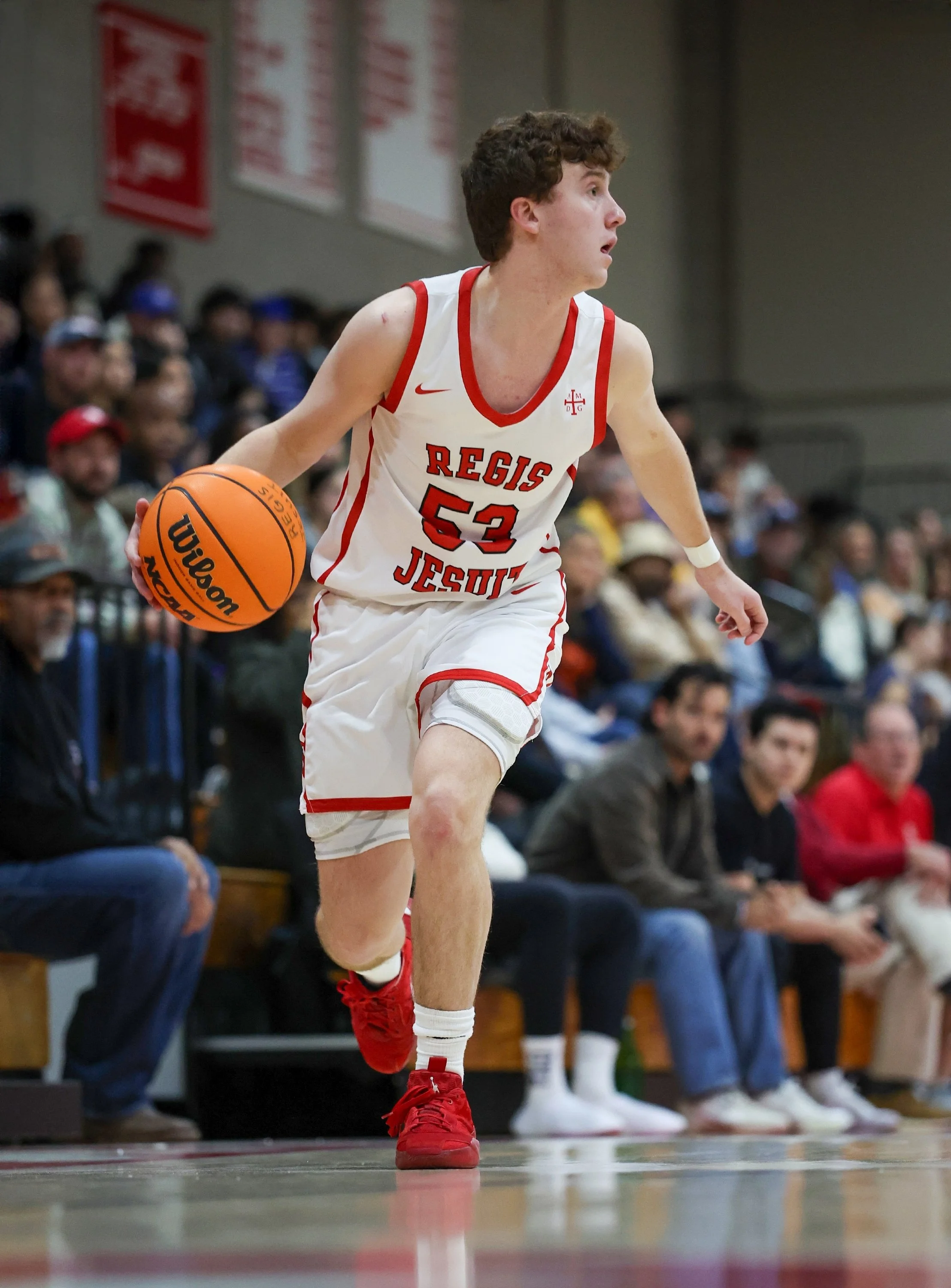Joseph Haubert dribbles past defenders in a Regis Jesuit High School basketball game, showcasing ball-handling, agility, and offensive creativity.