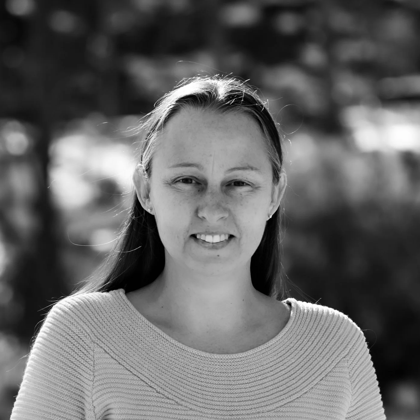 Black and white portrait of a young woman with long hair smiling outdoors.