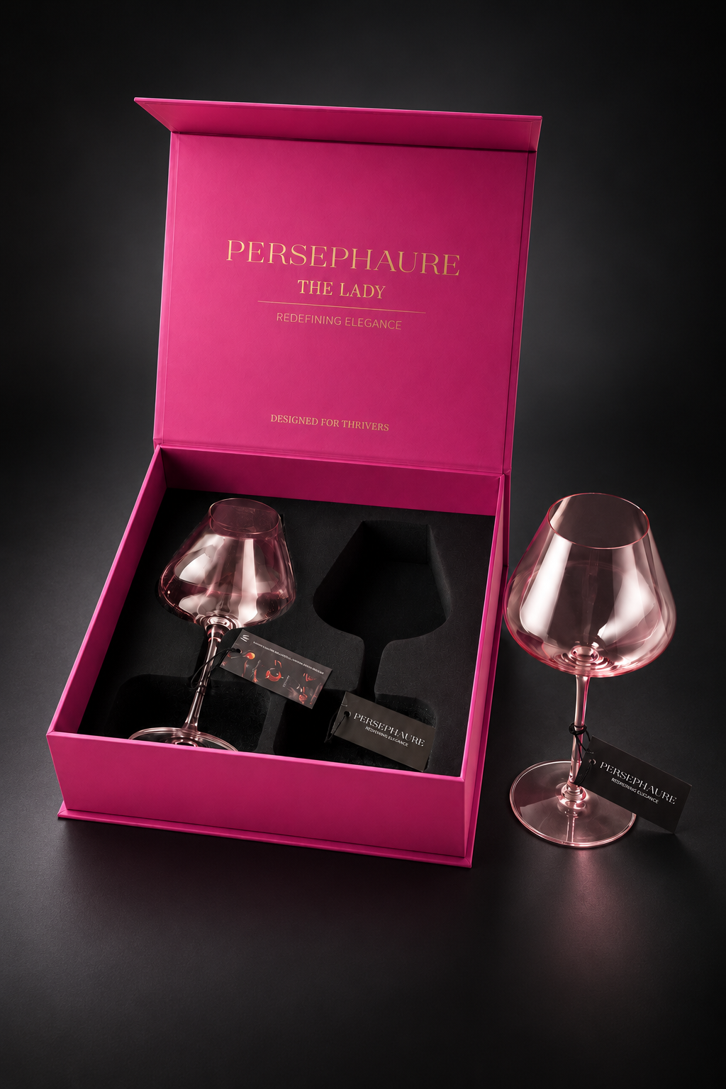 Pink Lady wine glass beside its open Persephaure gift box, with a second glass inside, on charcoal.