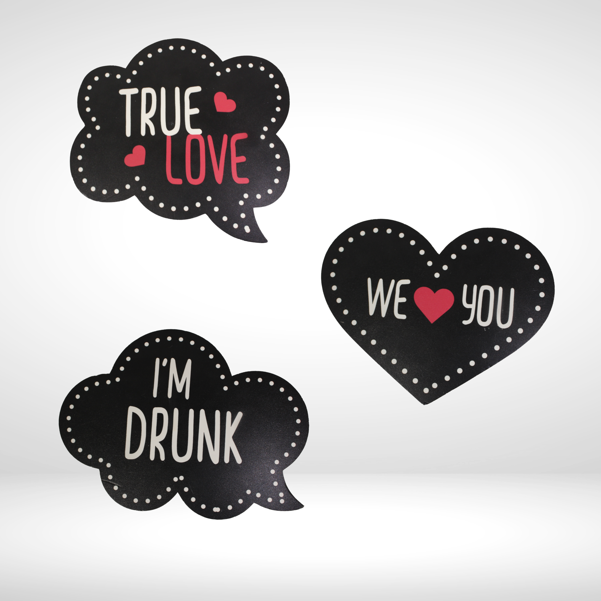 Three black speech bubble-shaped signs with white dotted borders, displaying phrases in colorful and white text: "True Love" with pink hearts, "We Love You" with a red heart, and "I'm Drunk".