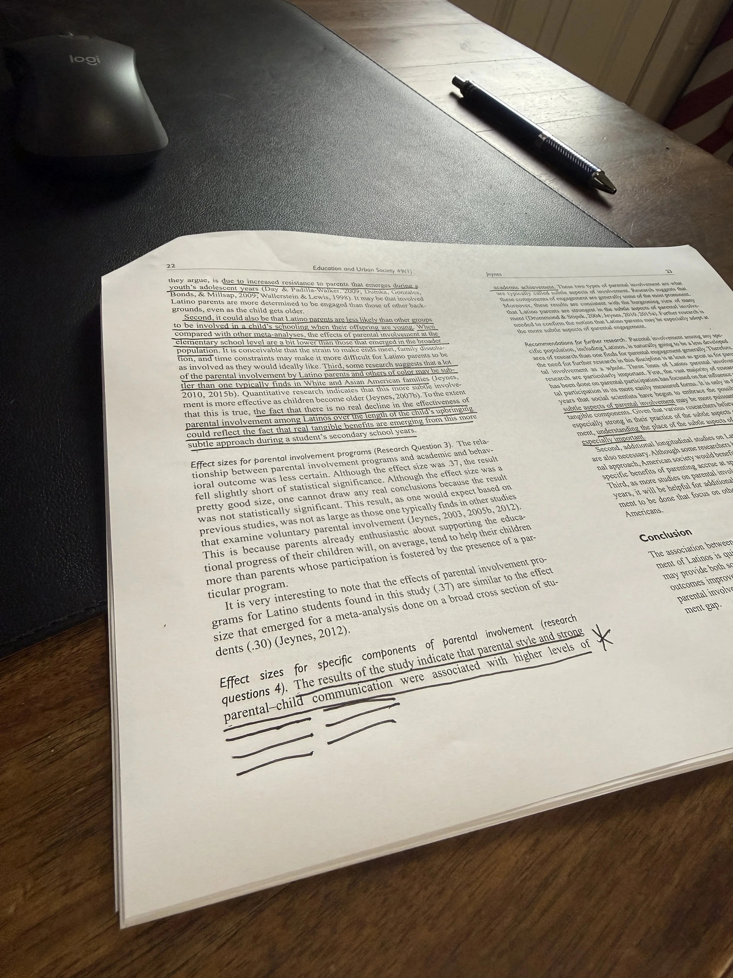 A printed document with highlighted text and handwritten notes, placed on a wooden table, with a pen and a wireless mouse nearby.