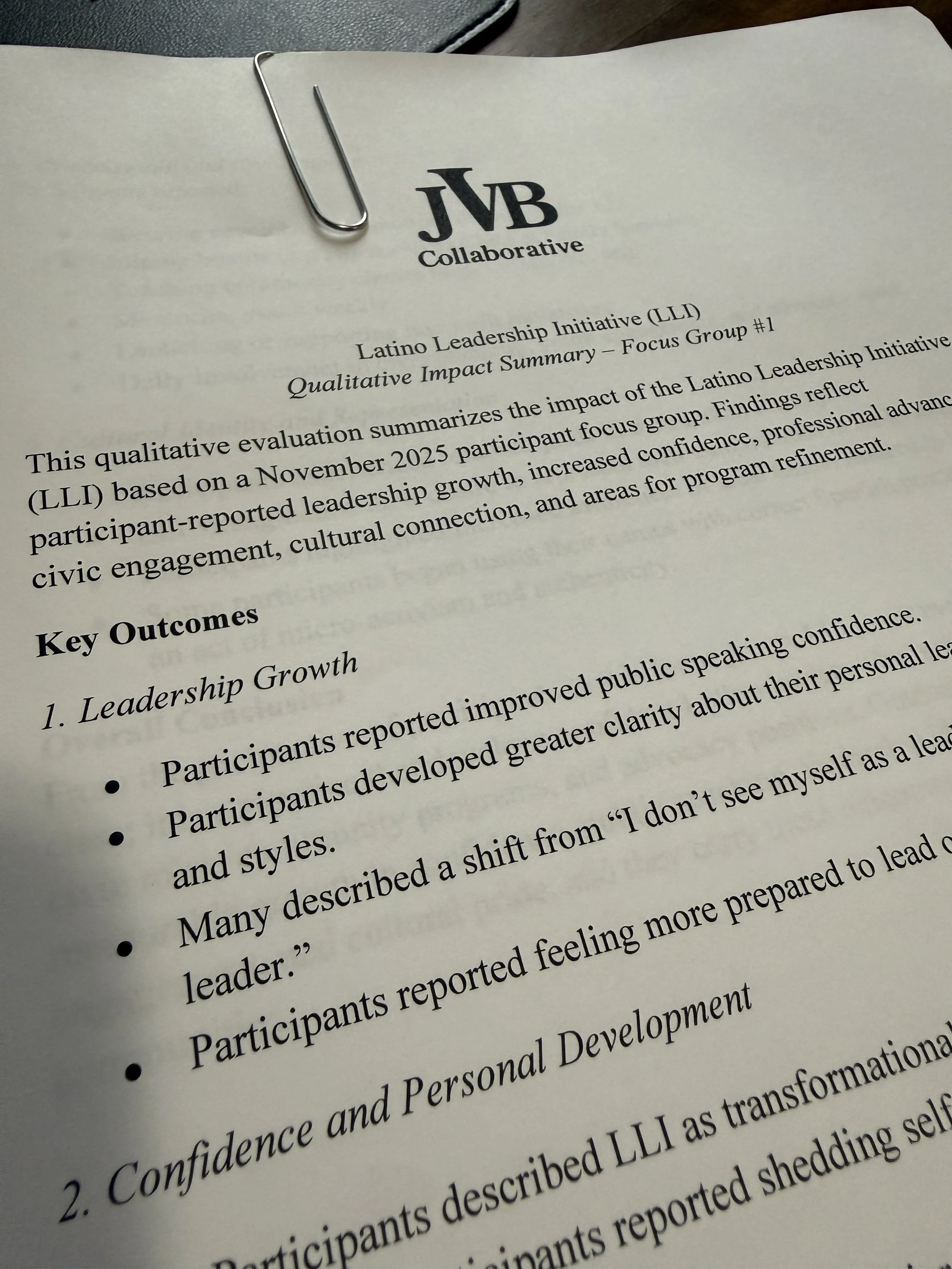 A printed report titled 'Latino Leadership Initiative (LLI) Qualitative Impact Summary - Focus Group #1' with a logo at the top reading 'JVB Collaborative.' The report is clipped with a large paperclip and discusses the impact of a leadership program, including key outcomes like leadership growth, confidence, and personal development.