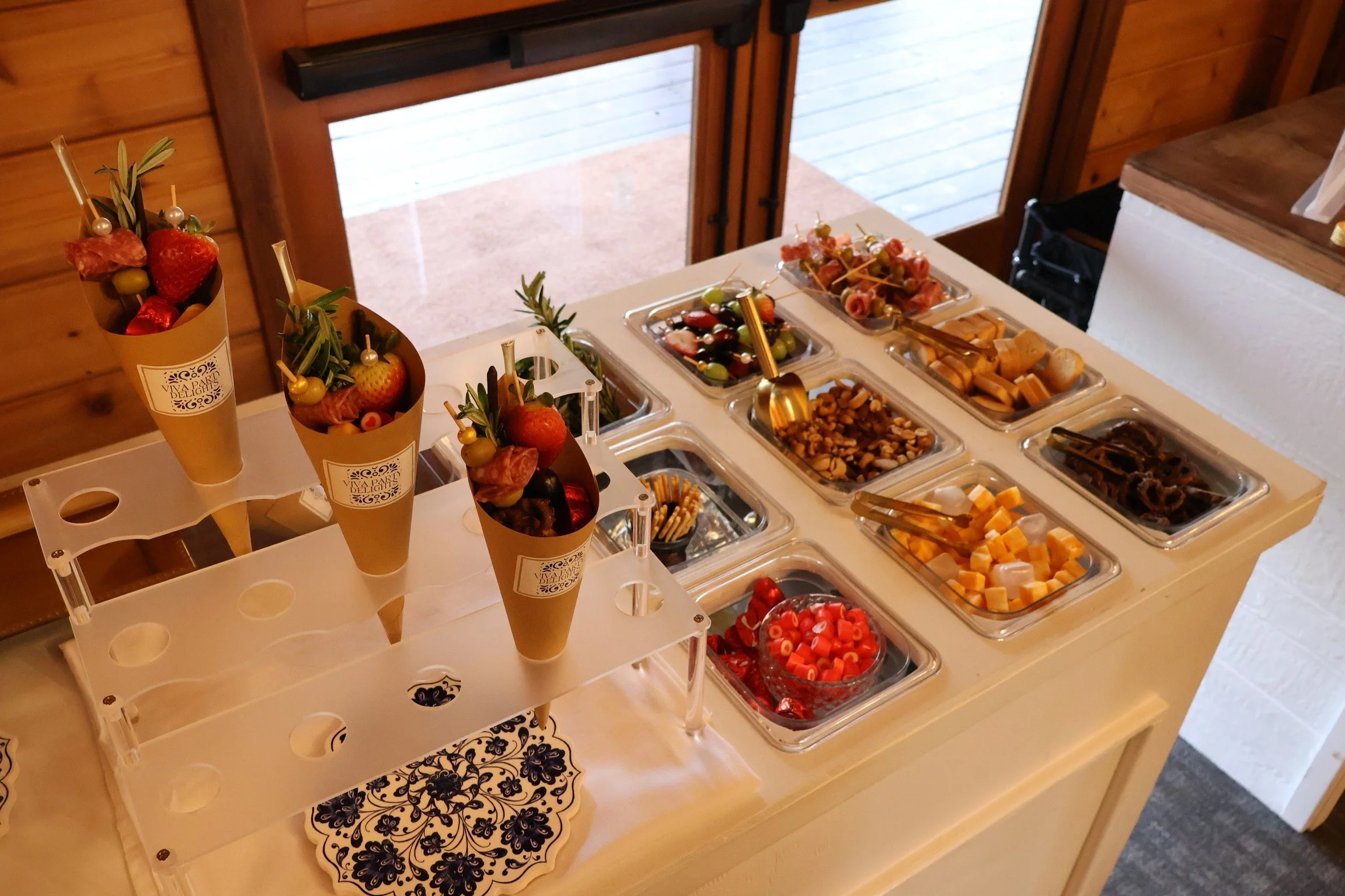 Charcuterie cones with assorted ingredients, including strawberries, olives, cheese, pretzels, crackers, and meats, displayed on a white counter with serving bins.