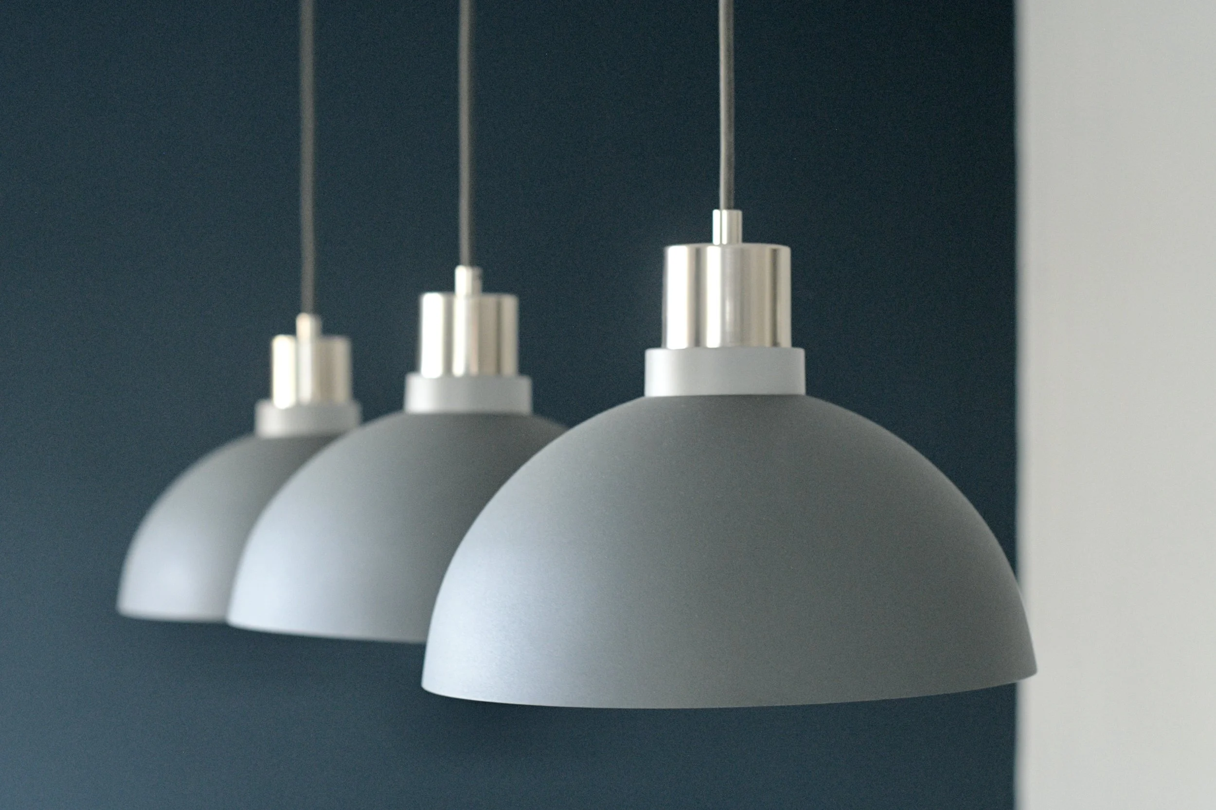 Close-up of three modern hanging pendant lamps with white shades and silver fixtures against a dark wall.