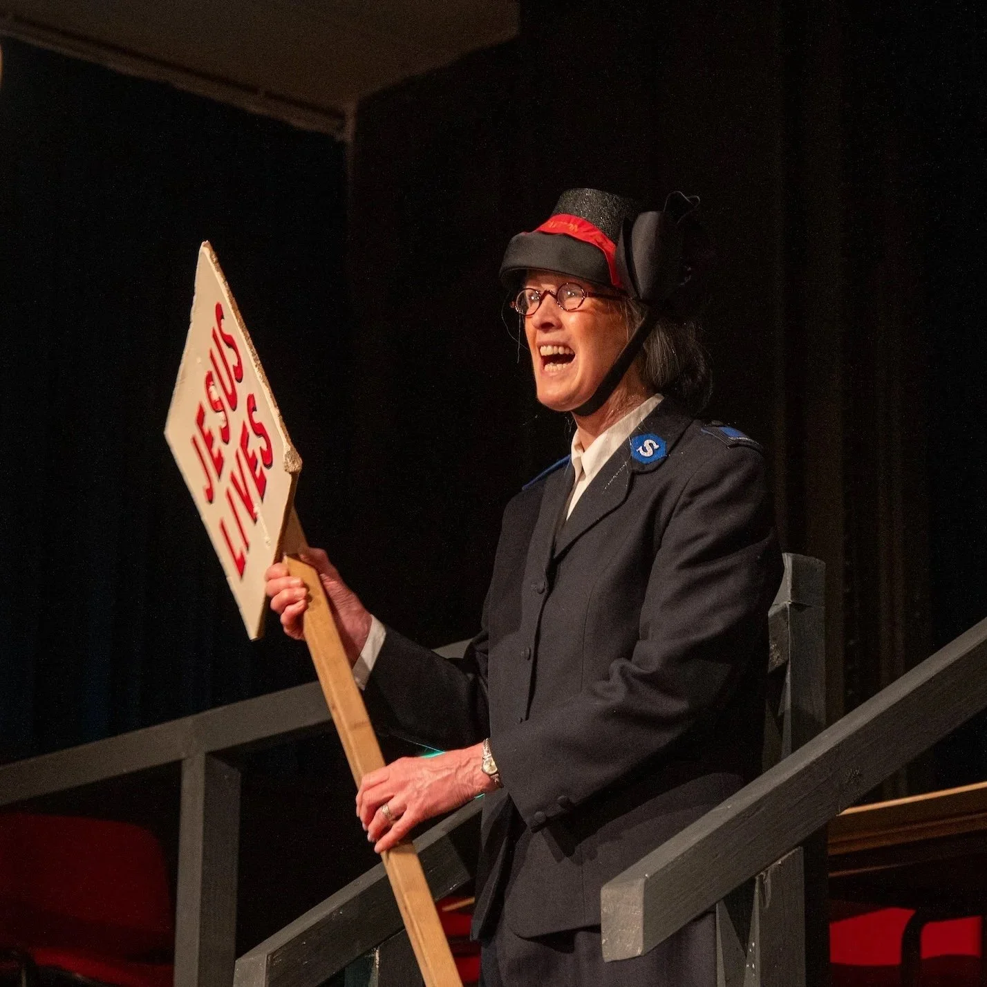 Drama scene: A woman in Salvation Army uniform, holding a religious sign.'