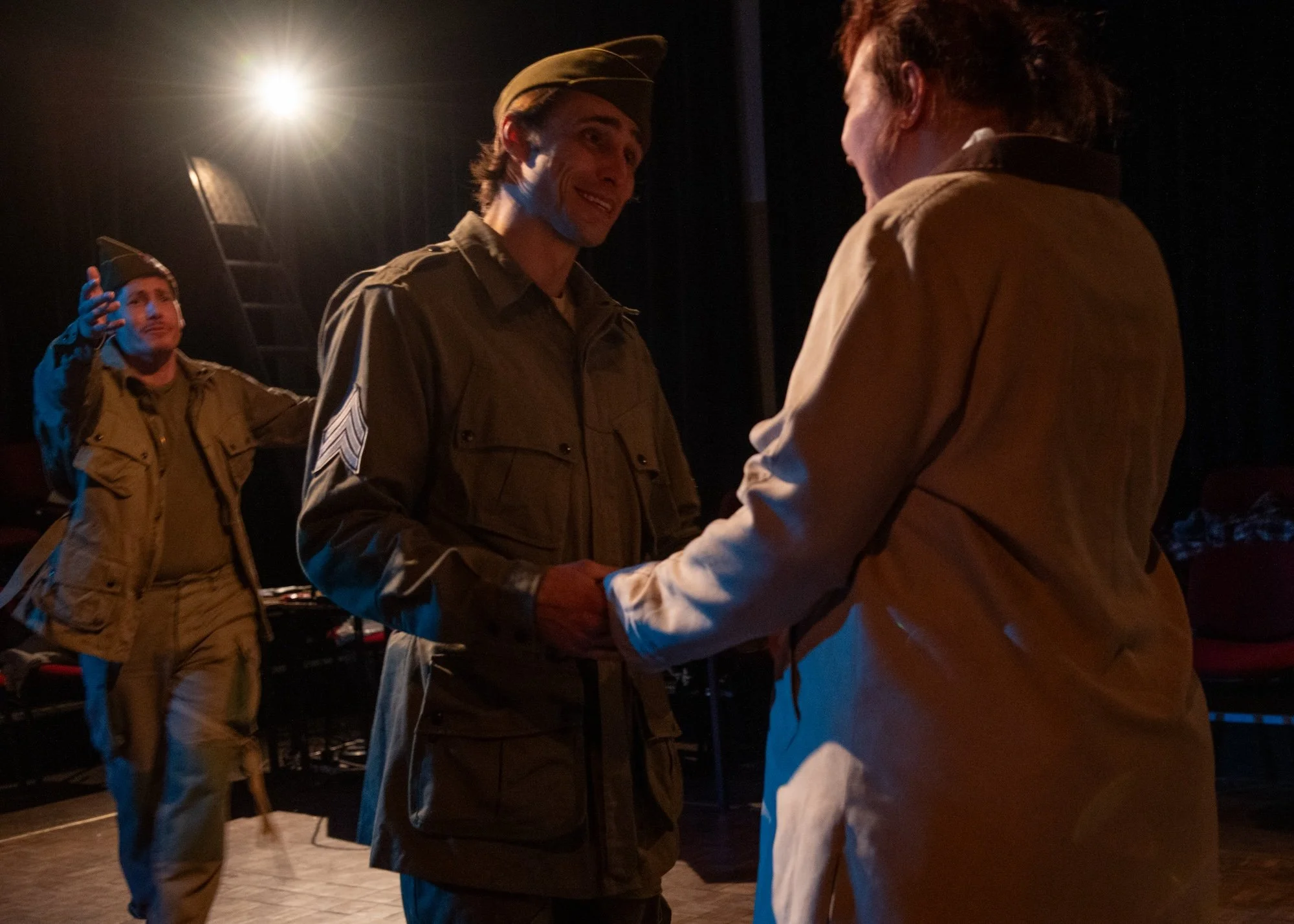 Drama scene: a foreground smiling couple, with a third man in the background trying to attract their attention.