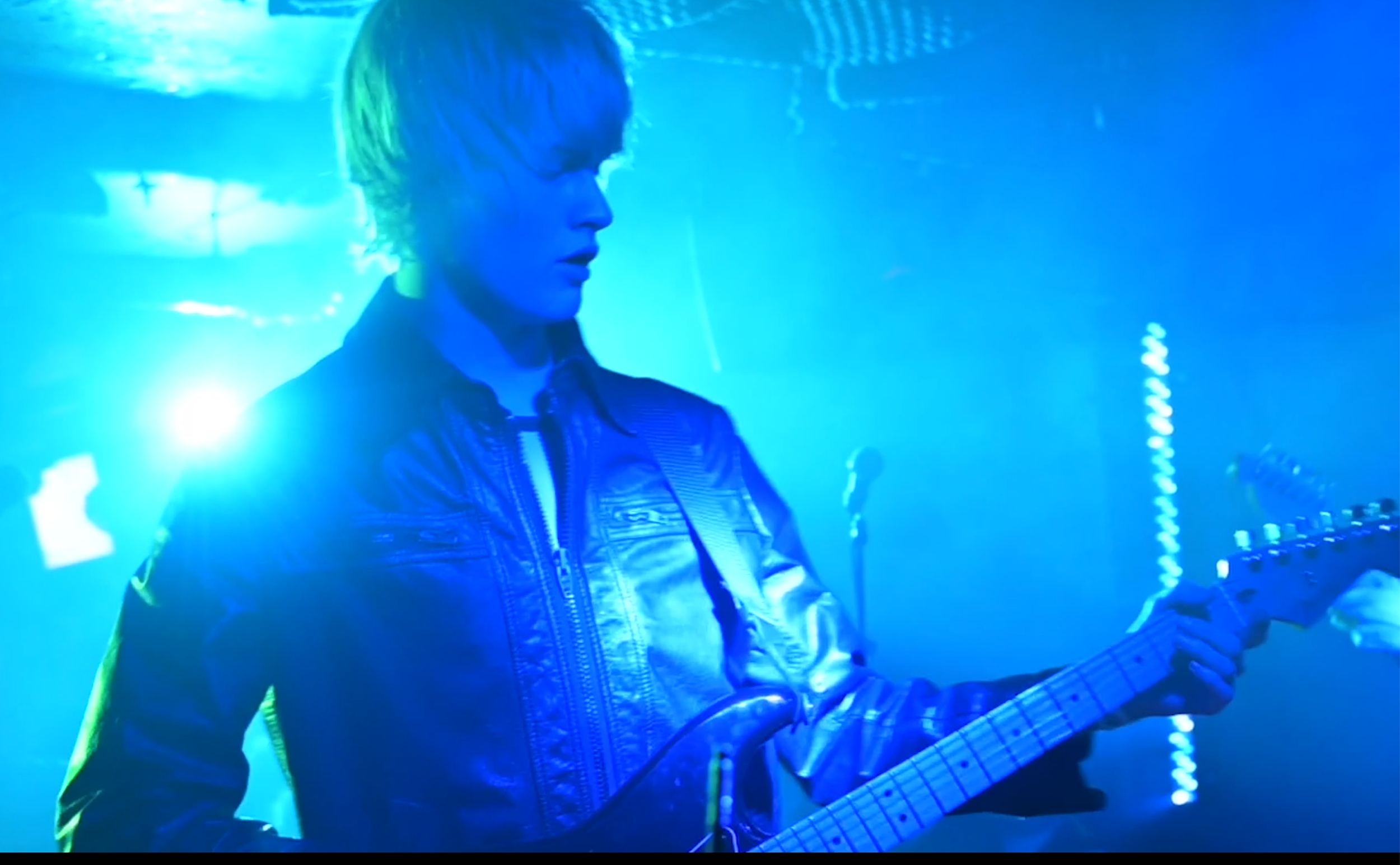 A guitarist onstage under blue stage lighting.
