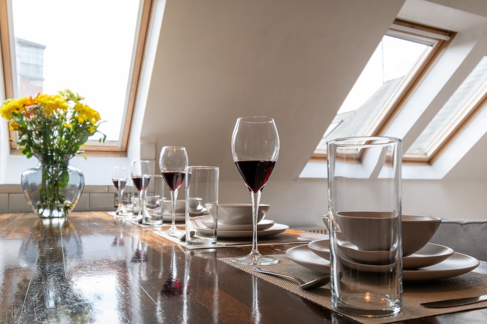 Set dining table with wine glasses, bowls, and plates, and a vase of yellow flowers in a room with skylight windows.