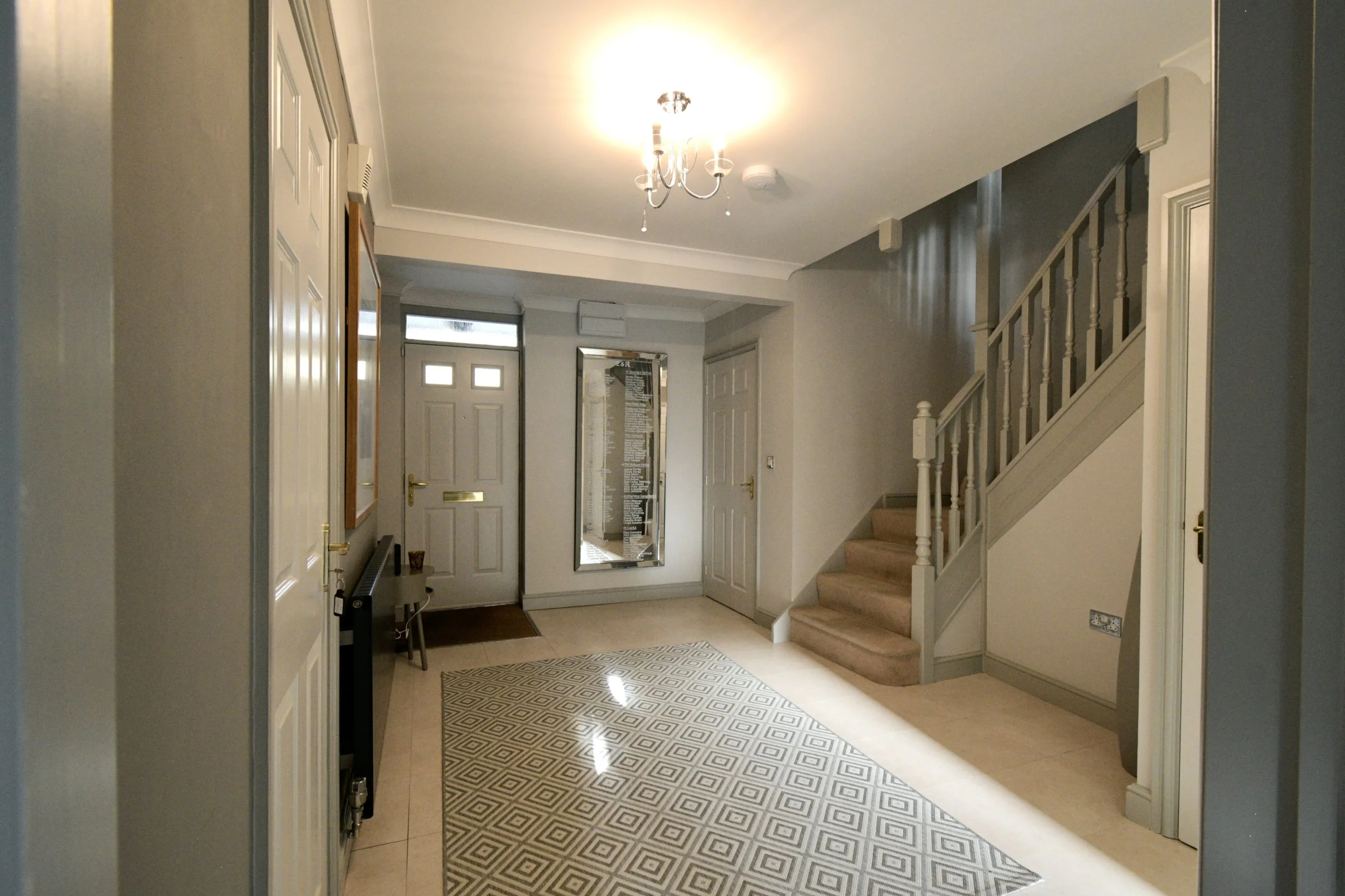 Entryway of a house with staircase, mirror, and front door, illuminated by ceiling light.