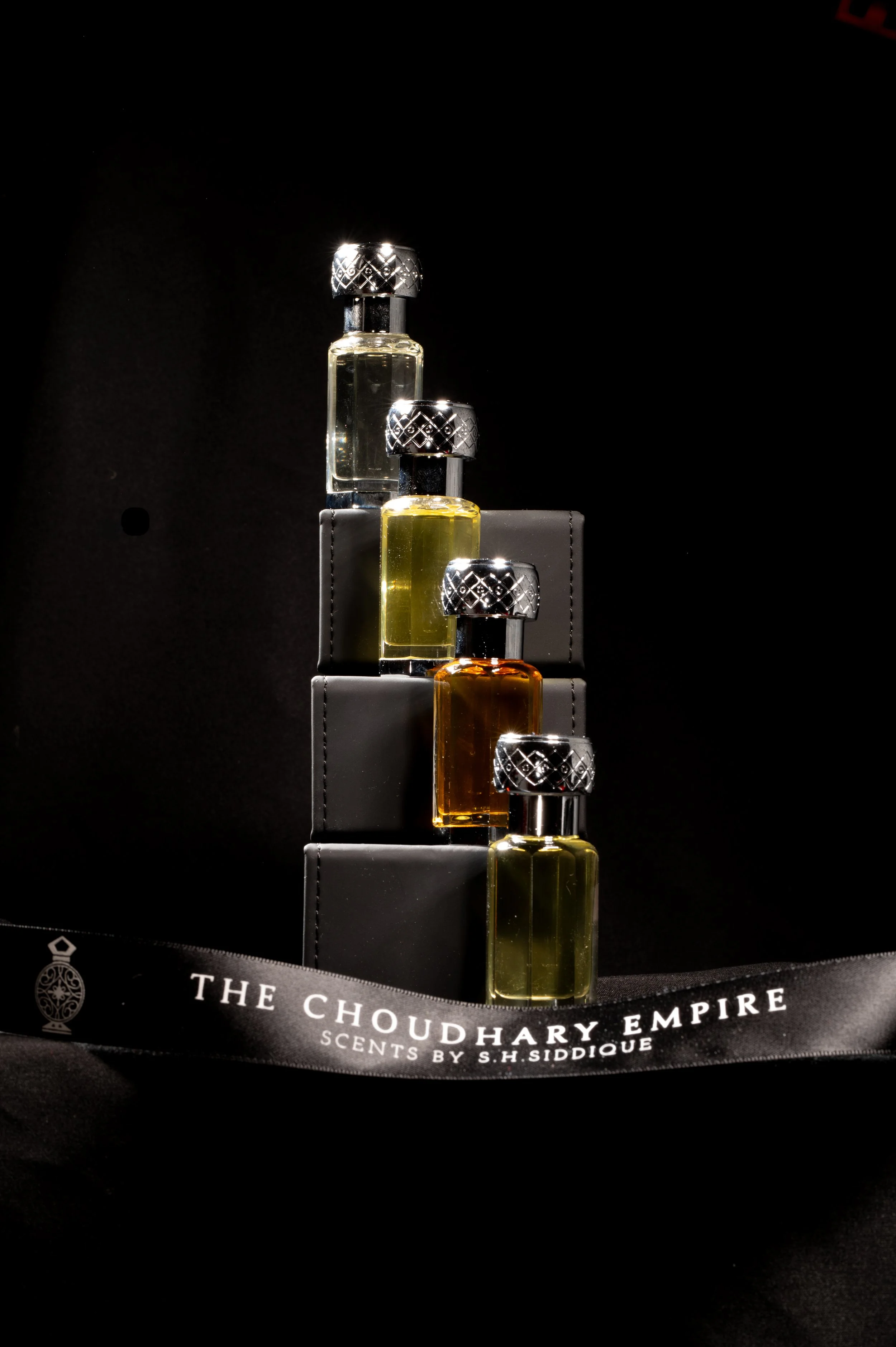 A display of small perfume bottles with metallic caps on a black background, arranged vertically on a stand