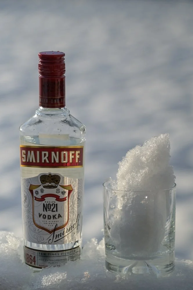 A bottle of Smirnoff vodka next to a glass filled with snow.