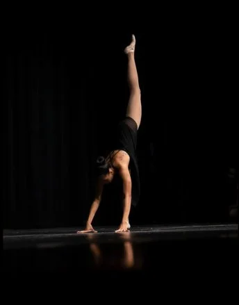 A dancer performing a handstand on a stage with a black background.