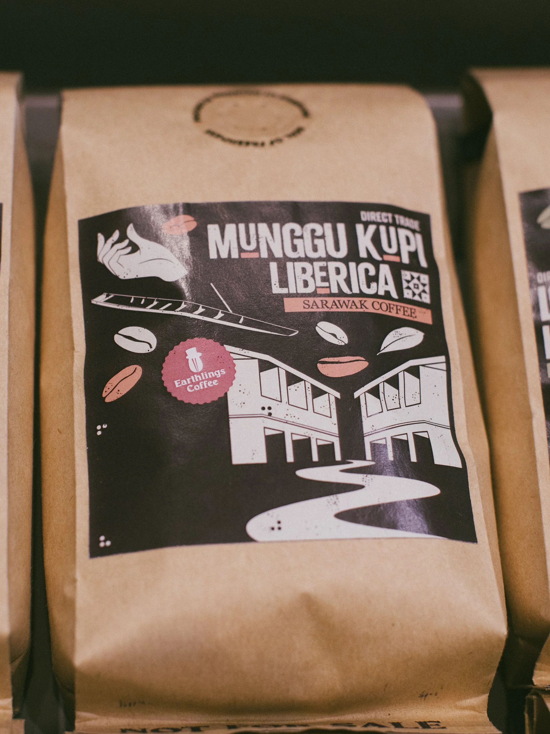 Bag of Munggu Kupi Liberica Sarawak coffee with illustrated buildings, coffee beans, a hand, and a steaming cup on the label.