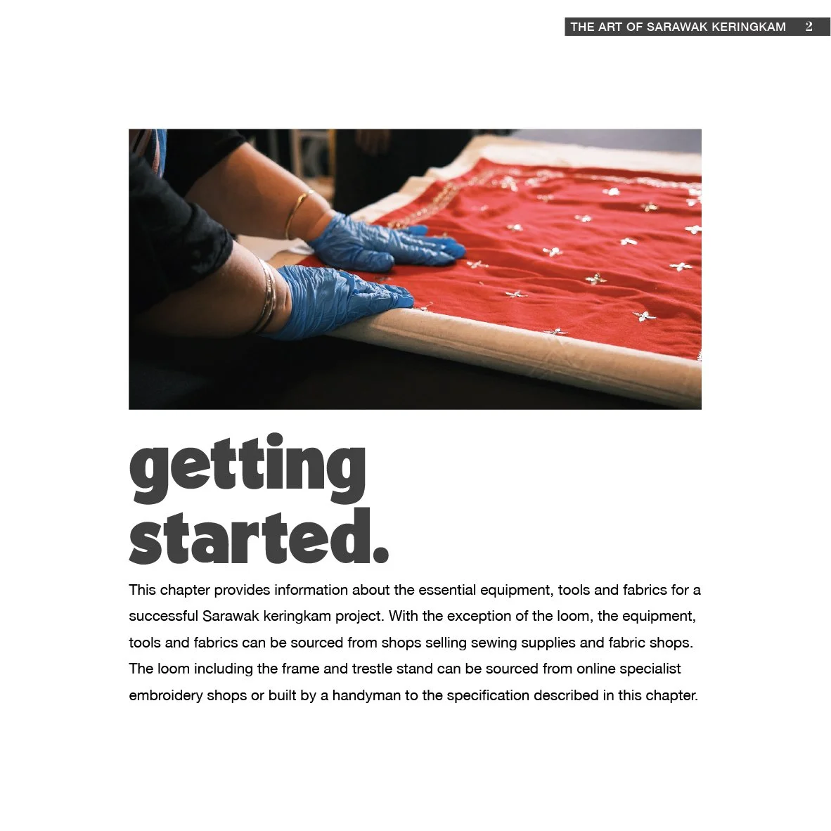 Close-up of hands in blue gloves handling a red fabric with embroidery, on a table.