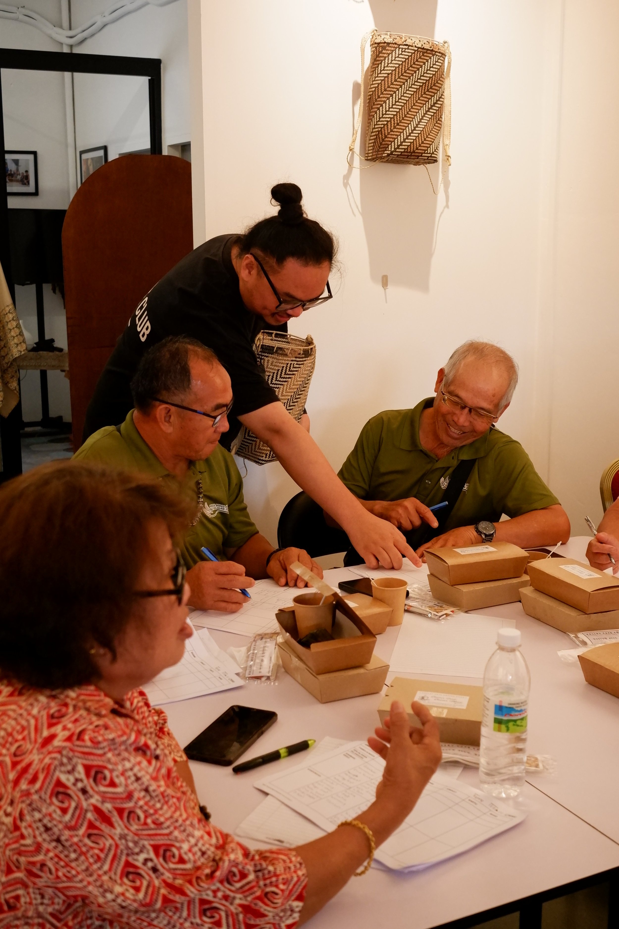 People sitting around a table with brown boxes, papers, and a water bottle, participating in a discussion or meeting.