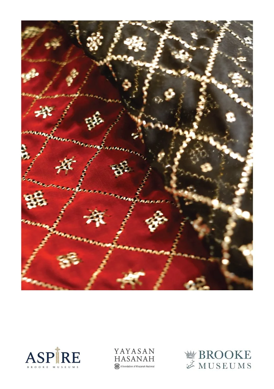 A close-up of embroidered fabric with a black and red color scheme, featuring a gold grid pattern and small decorative motifs.