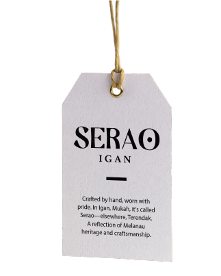 A white tag with the text 'SERAO IGAN' and a description about craftsmanship and heritage, hanging from a gold string.