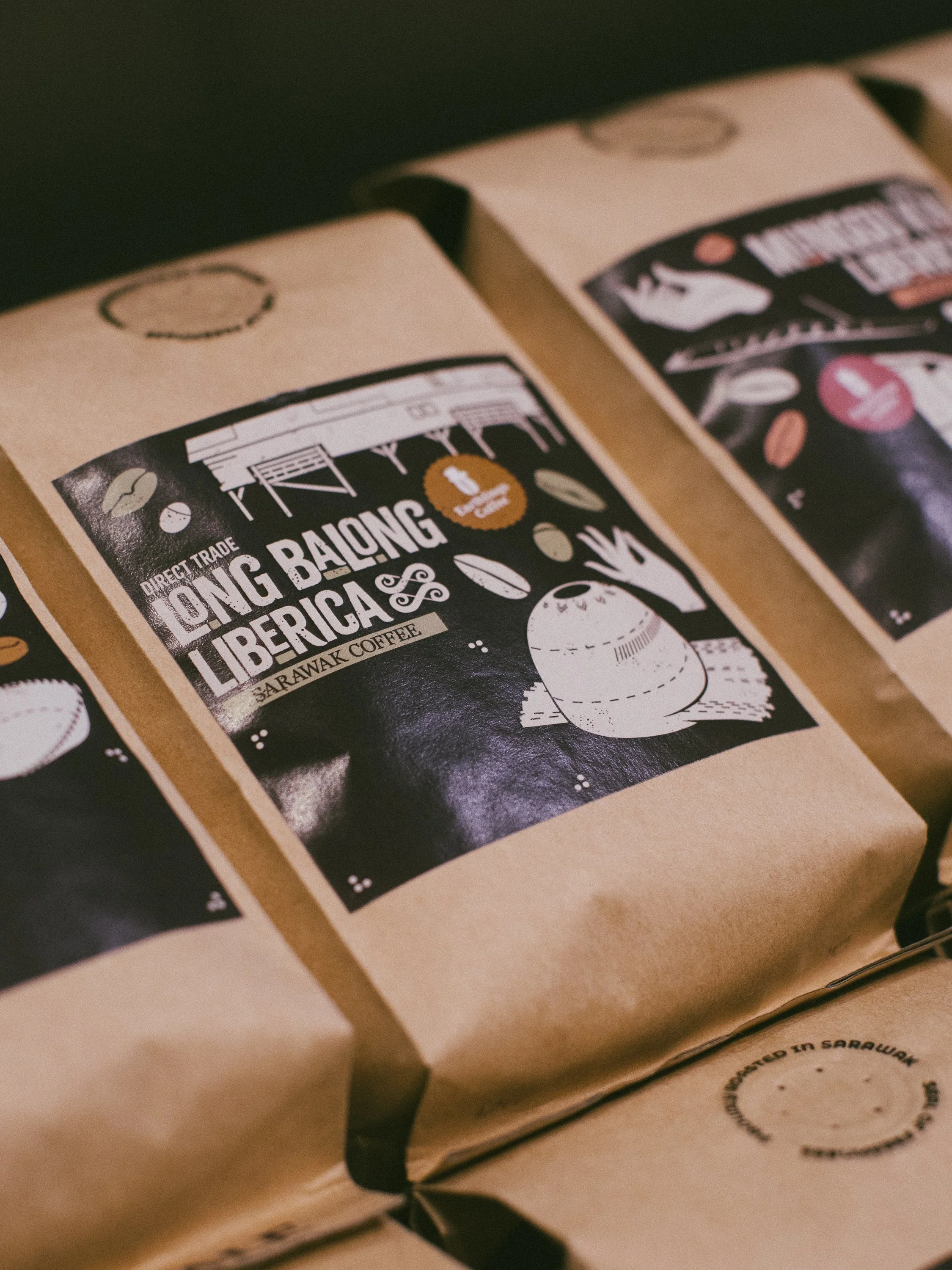 Brown paper bags of coffee labeled 'Long Bailing Liberia' with a graphic of a coffee bean and a coffee cup.