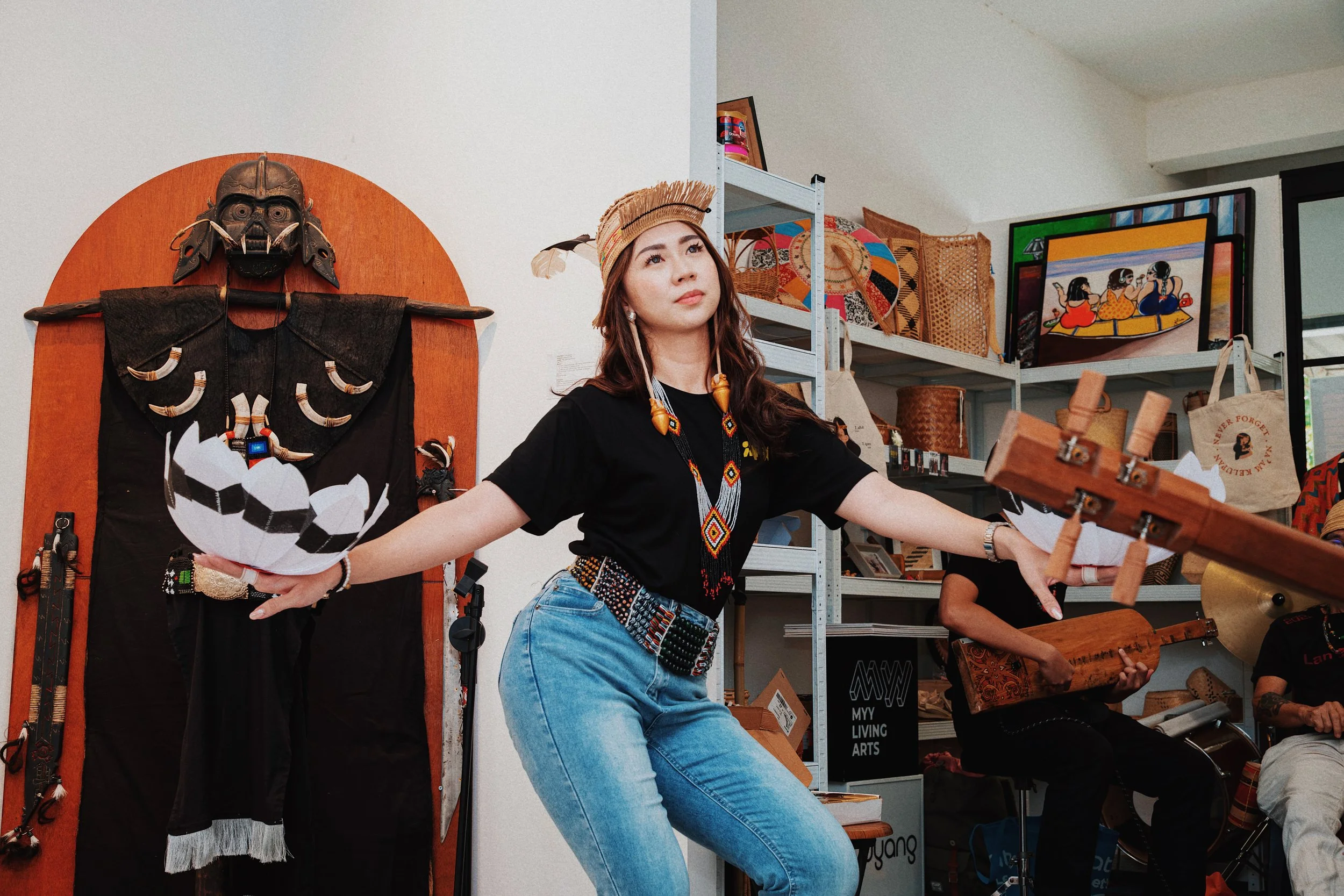 Woman in traditional Indigenous attire performing a dance or song in an art gallery with Indigenous artwork and crafts around her.