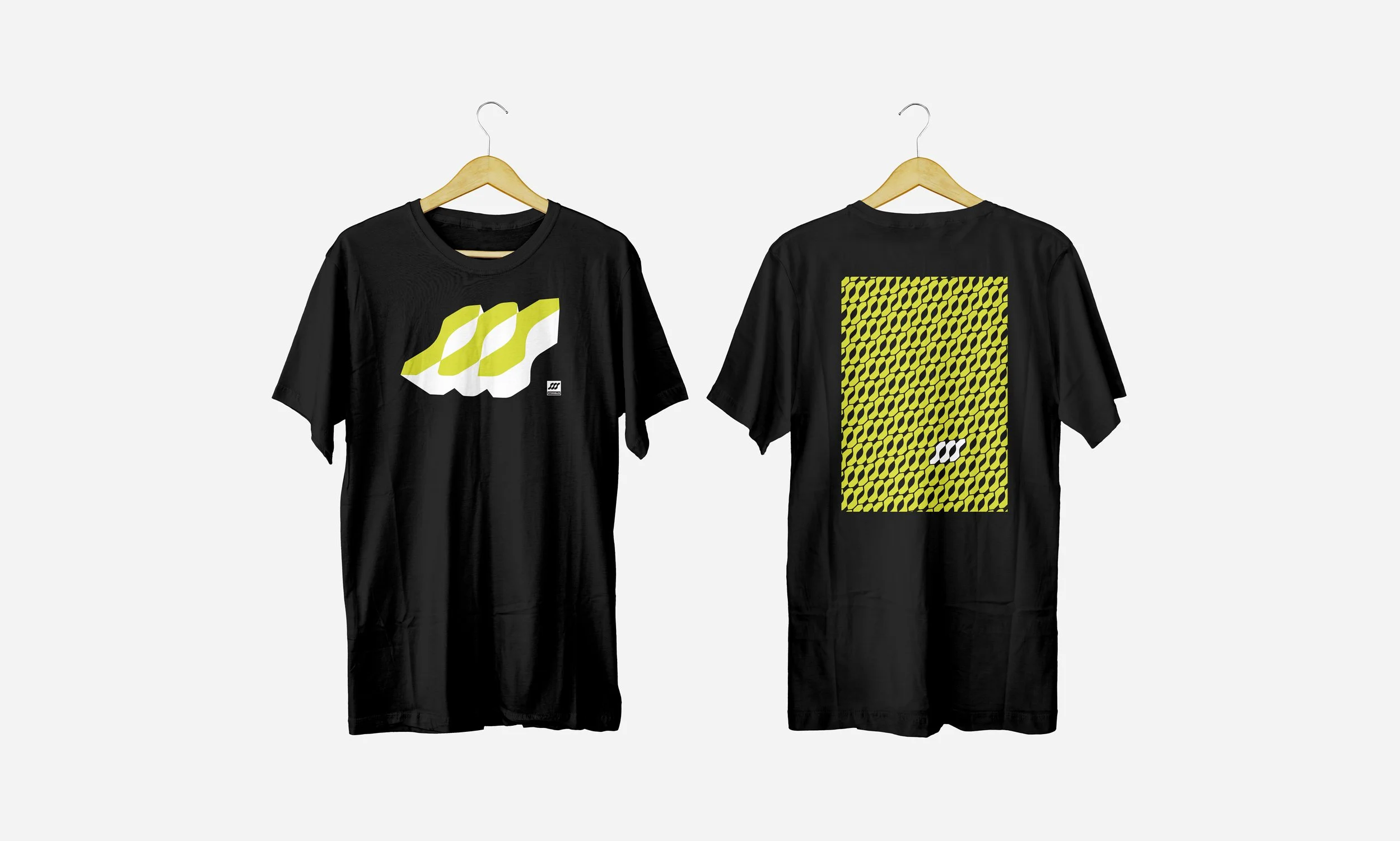 Two black T-shirts hanging on wooden hangers, one showing a large graphic of four overlapping yellow and white 'M' shapes on the front, and the other displaying a pattern of small yellow and black 'M' shapes with a small logo in the center of the back.
