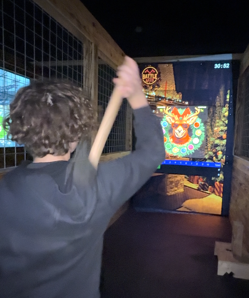Person with curly hair wearing a dark hoodie hitting a digital archery target with an axe.