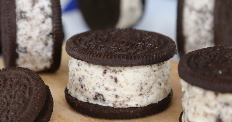 Oreo cookie ice cream sandwich with cookies and ice cream layered between two Oreo cookies on a wooden surface, with other Oreo cookies in the background.