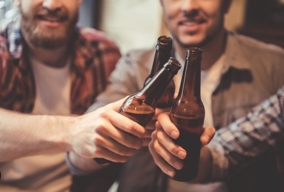 Four friends clinking beer bottles in a toast indoors.