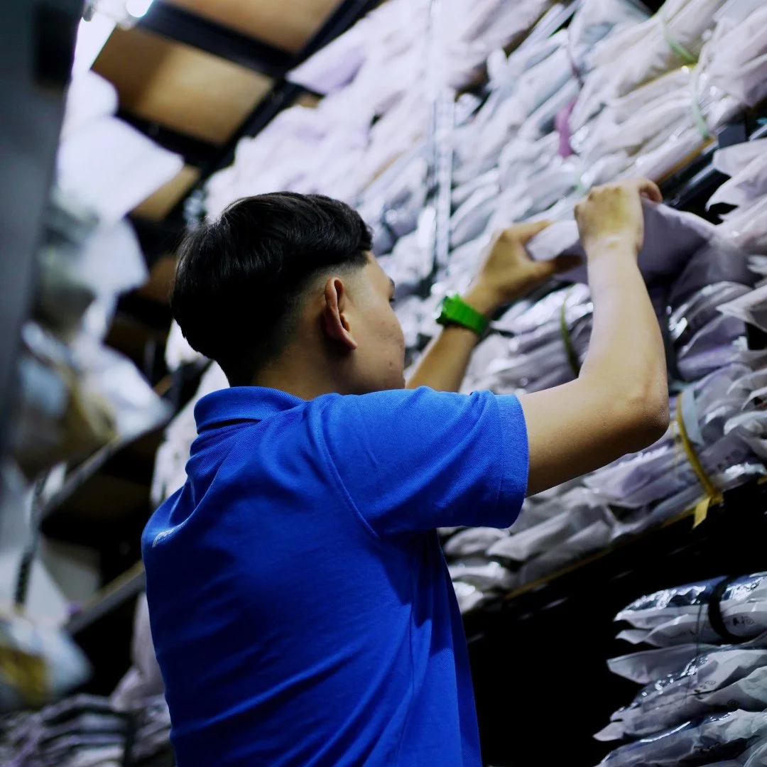 Person in a blue shirt organizing stacked packages on shelves.