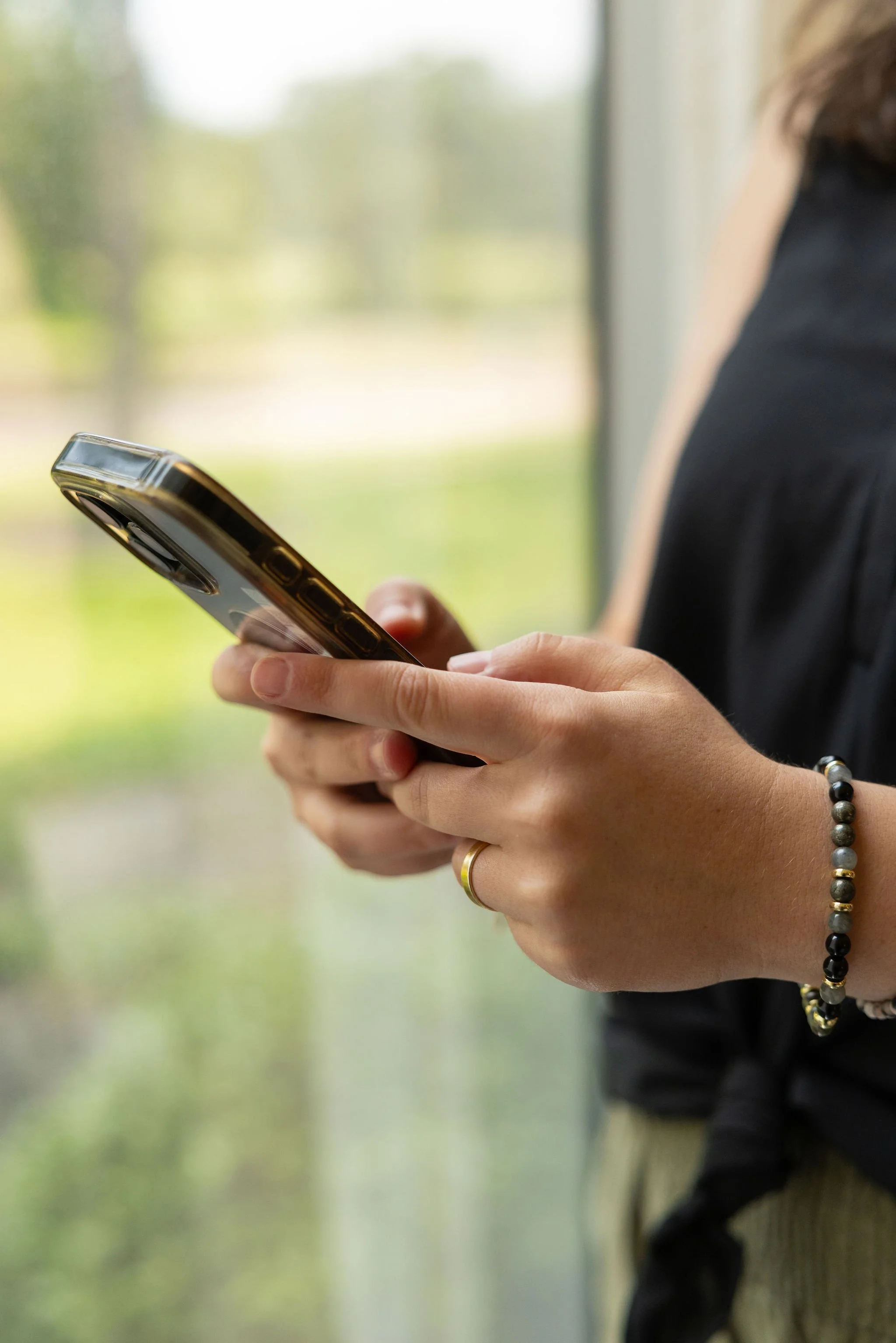 Person holding a smartphone with a blurred green outdoor background.
