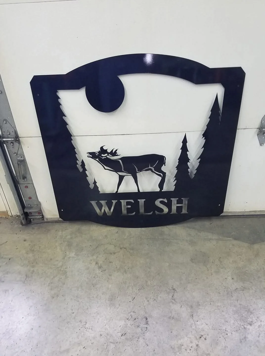 Metal wall art depicting a moose silhouette, trees, a full moon, and the word "WELSH."