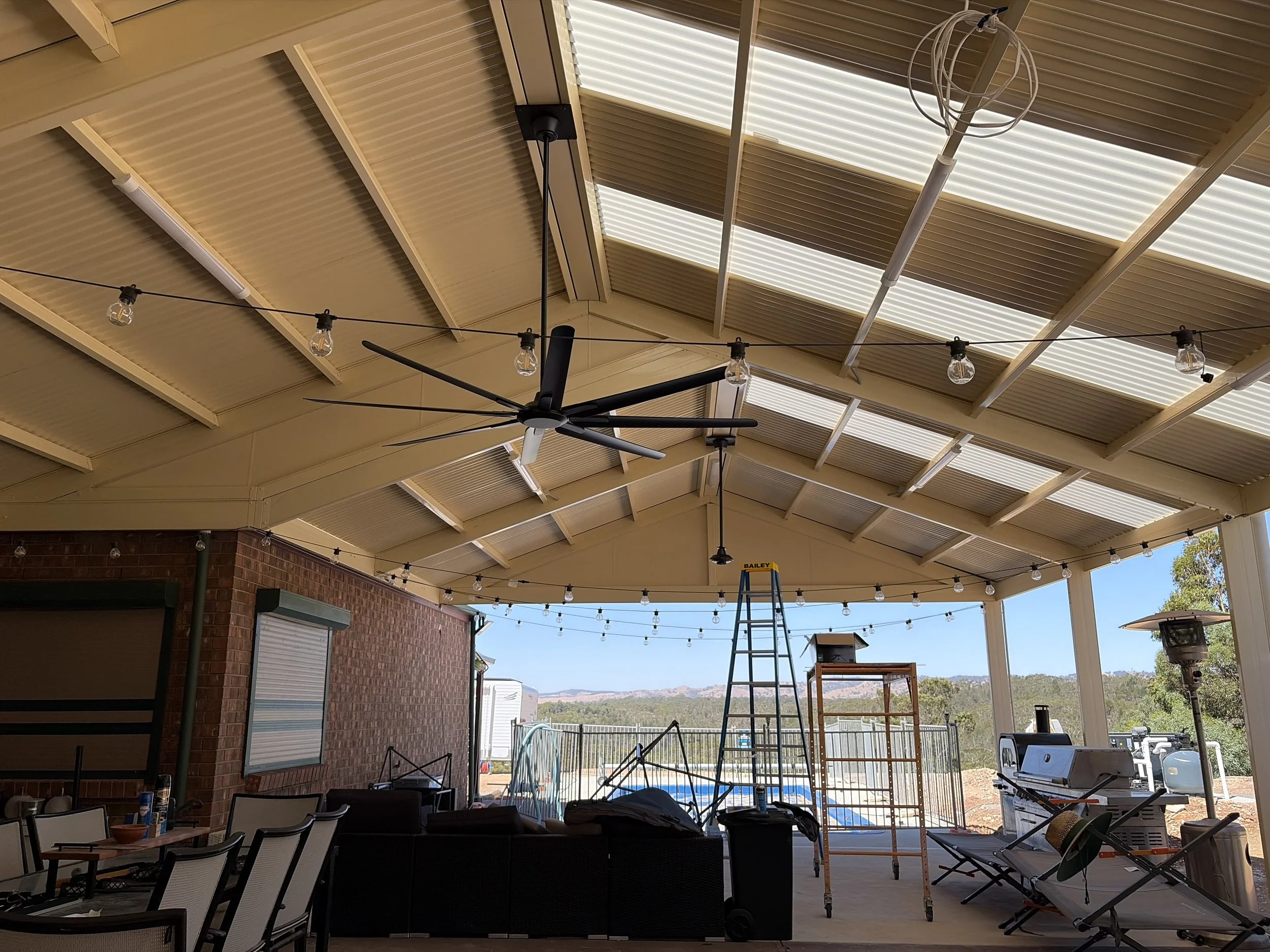 Black outdoor fan in undercover area, it is large with 8 blades, in the background is a beautiful view