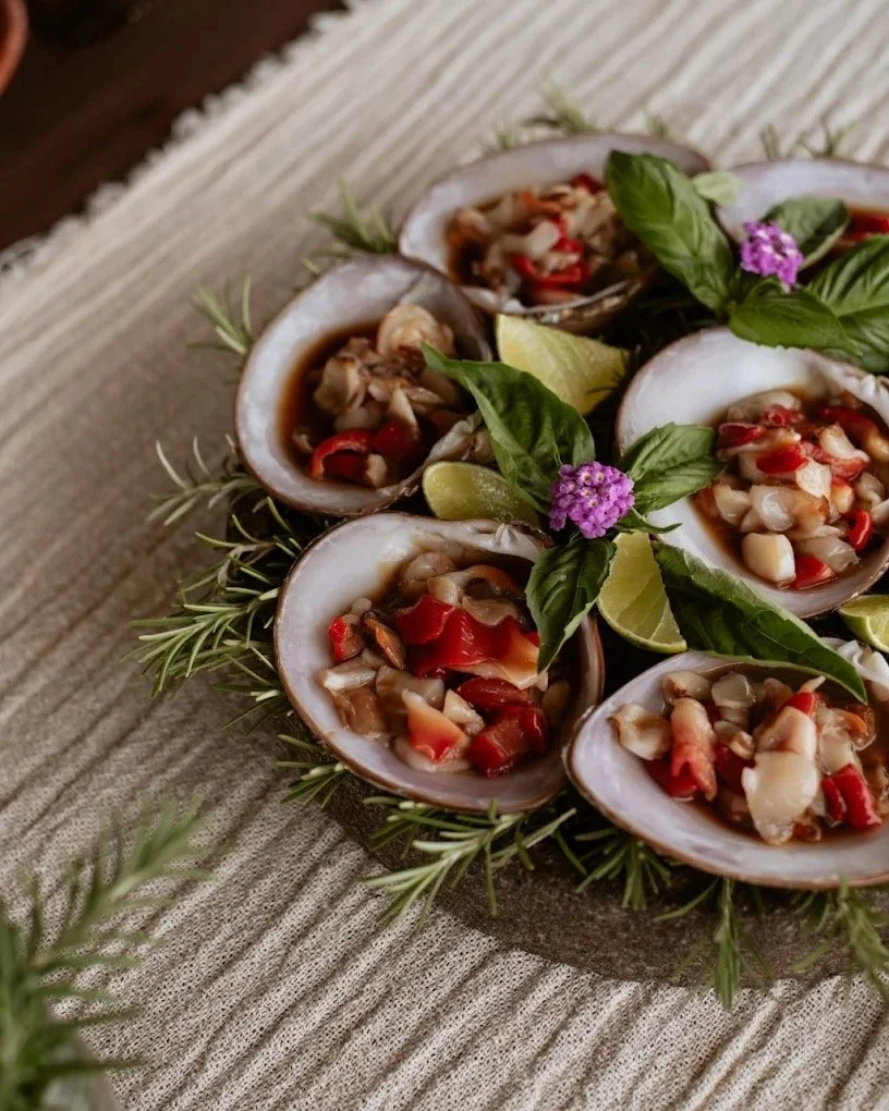 Top view of a platter of stuffed clams garnished with fresh herbs and lime wedges, placed on a textured cloth surface.