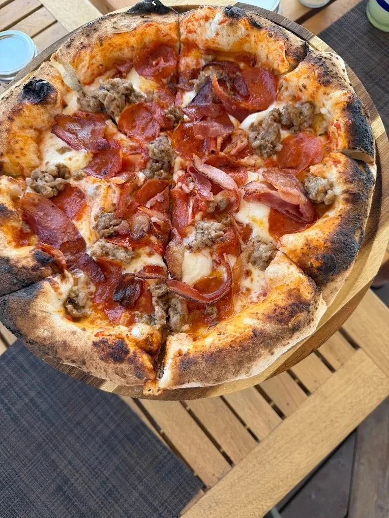 A pizza with pepperoni, bacon, sausage, and cheese on a wooden pizza board.