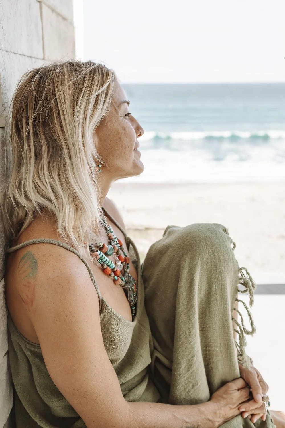 Agathe Fay sitting by a East Cape Baja beach, looking out to sea, wearing a green dress with layered necklaces.