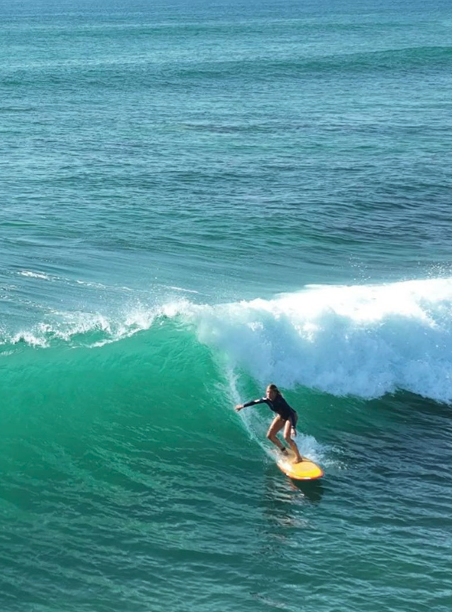 A person surfing on a yellow surfboard on a turquoise wave in the ocean.