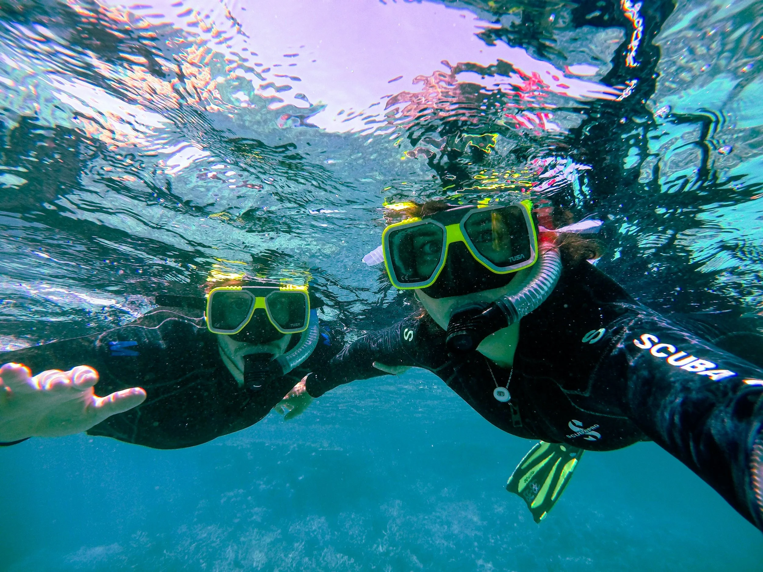 Underwater photo of two scuba divers with yellow and black masks, surrounded by clear blue water, and sunlight filtering through the surface.