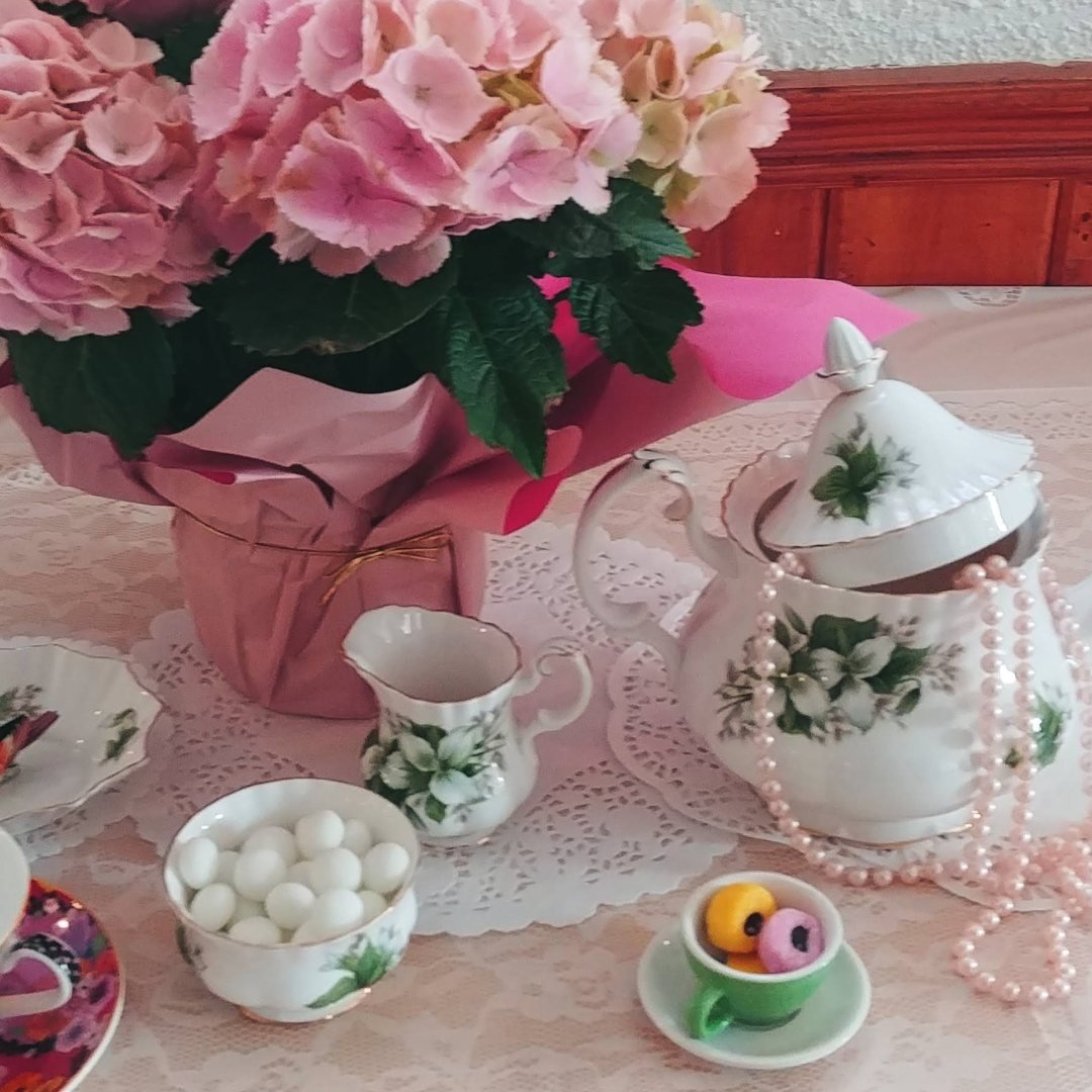Floral teapot set with pink flowers and lace tablecloth.