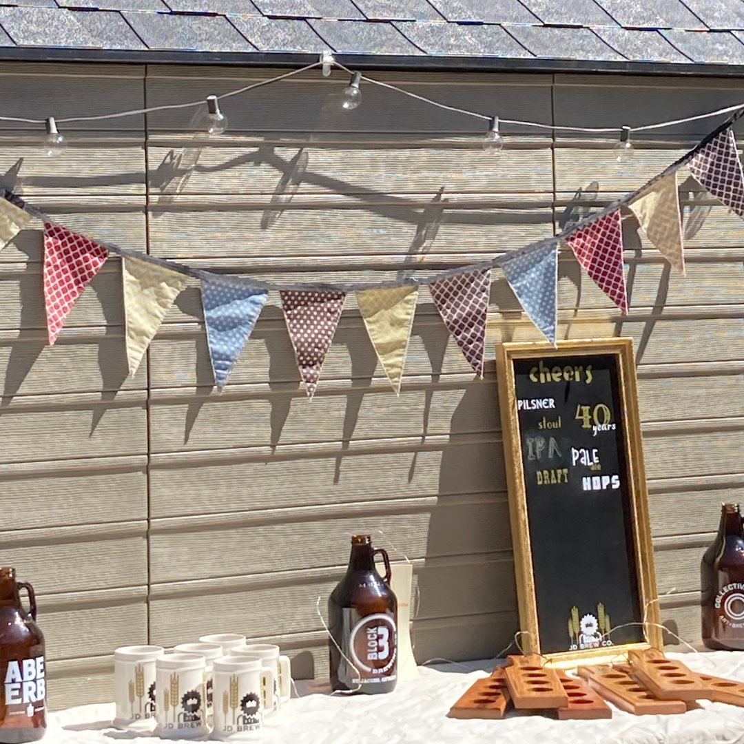 Outdoor party setup with a variety of beer-related items, including a chalkboard menu, beer growlers, cups, decorative bunting, and string lights.