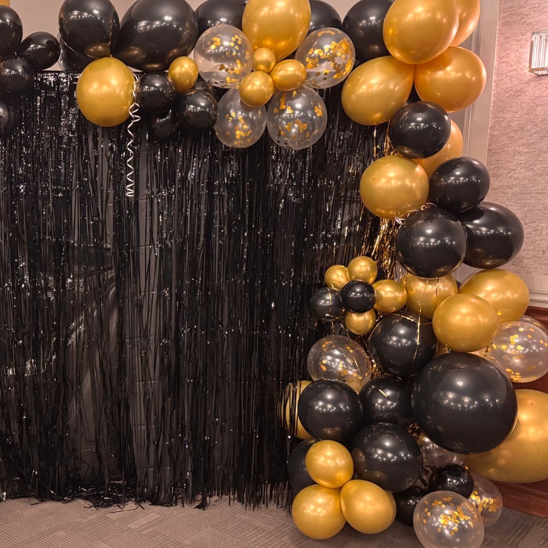 Black and gold balloon arch with black tinsel backdrop