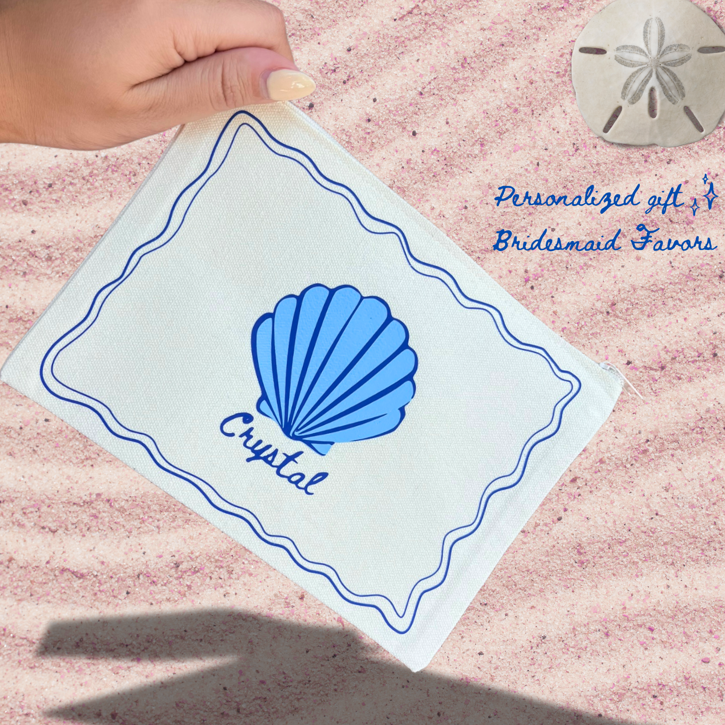 A close-up of a hand holding a personalized pouch with 'Crystal' written on it, featuring a blue seashell design. The background is sandy with a sand dollar and text reading 'Personalized gift Bridesmaid Favors.'